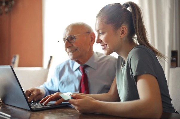A young woman and an old man making a payment on a laptop.